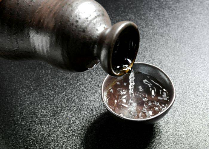 A dark ceramic sake bottle pouring sake into a cup of the same material.